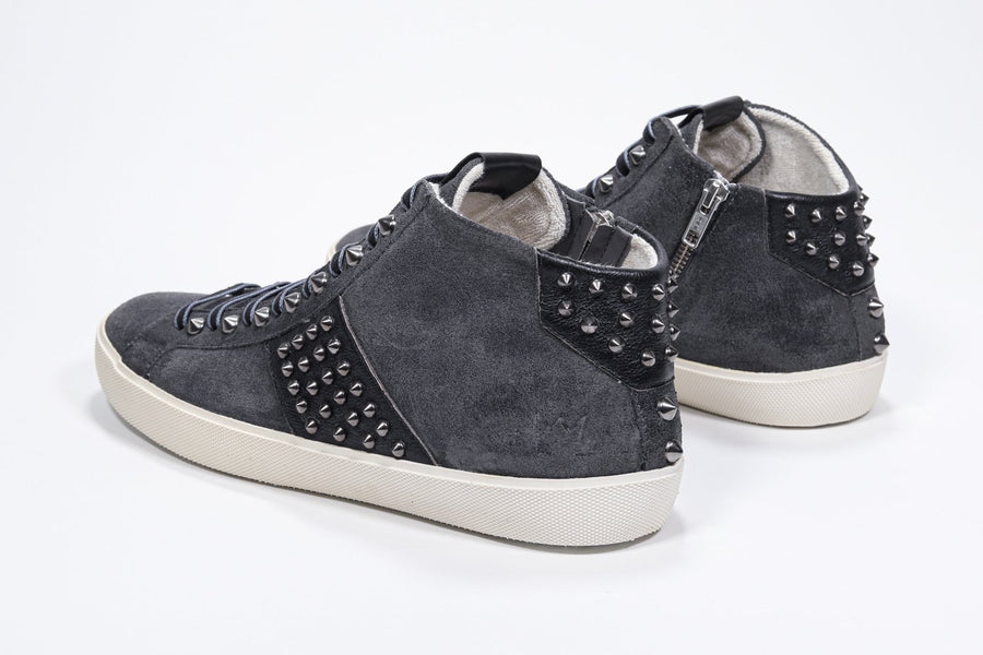 Three quarter back view of mid top dark grey sneaker. Suede and leather upper with studs, an internal zip and vintage rubber sole.