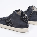 Three quarter back view of mid top navy sneaker. Suede and leather upper with studs, an internal zip and vintage rubber sole.