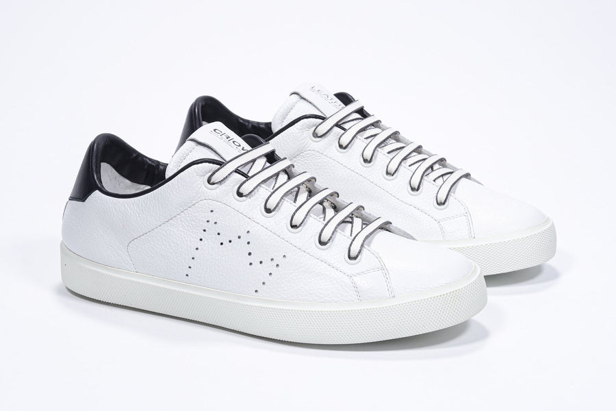 Three quarter front view of low top white sneaker with black detailing and perforated crown logo on upper. Full leather upper and white rubber sole.