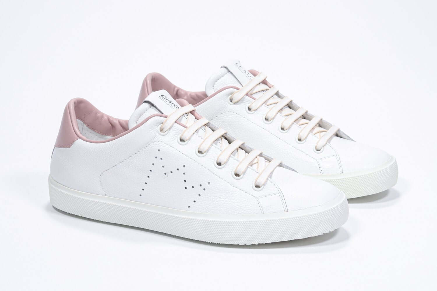 Three quarter front view of low top white sneaker with pale pink detailing and perforated crown logo on upper. Full leather upper and white rubber sole.