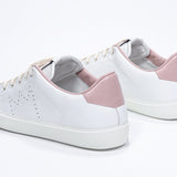 Three quarter back view of low top white sneaker with pale pink detailing and perforated crown logo on upper. Full leather upper and white rubber sole.