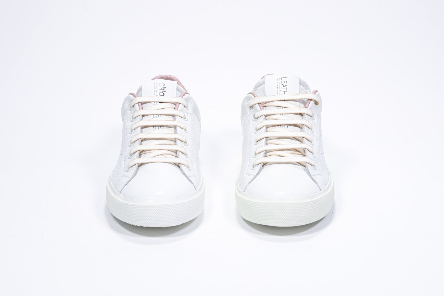 Vue de face de la chaussure blanche sneaker avec des détails rose pâle et le logo perforé de la couronne sur l'empeigne. Tige en cuir et semelle en caoutchouc blanc.