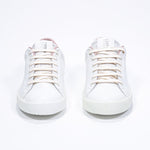 Front view of low top white sneaker with pale pink detailing and perforated crown logo on upper. Full leather upper and white rubber sole.