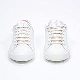 Front view of low top white sneaker with pale pink detailing and perforated crown logo on upper. Full leather upper and white rubber sole.