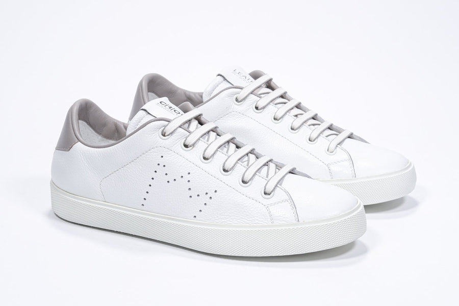 Three quarter front view of low top white sneaker with stone color detailing and perforated crown logo on upper. Full leather upper and white rubber sole.