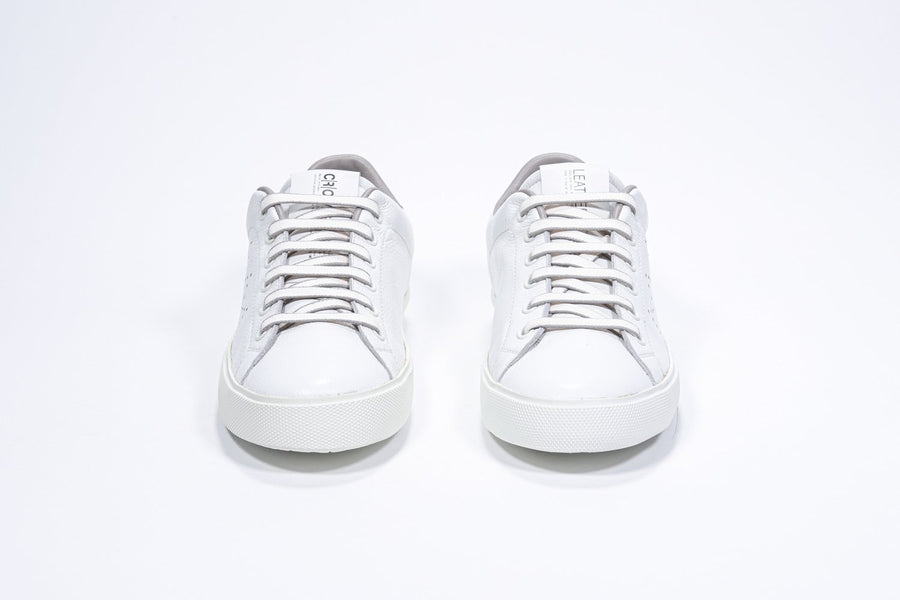 Front view of low top white sneaker with stone color detailing and perforated crown logo on upper. Full leather upper and white rubber sole.