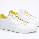Tre quarti di BASSE  sneaker  bianco con dettagli gialli e logo della corona traforato sulla tomaia. Tomaia in pelle e suola in gomma bianca.