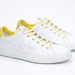 Three quarter front view of low top white sneaker with yellow detailing and perforated crown logo on upper. Full leather upper and white rubber sole.