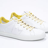 Three quarter front view of low top white sneaker with yellow detailing and perforated crown logo on upper. Full leather upper and white rubber sole.