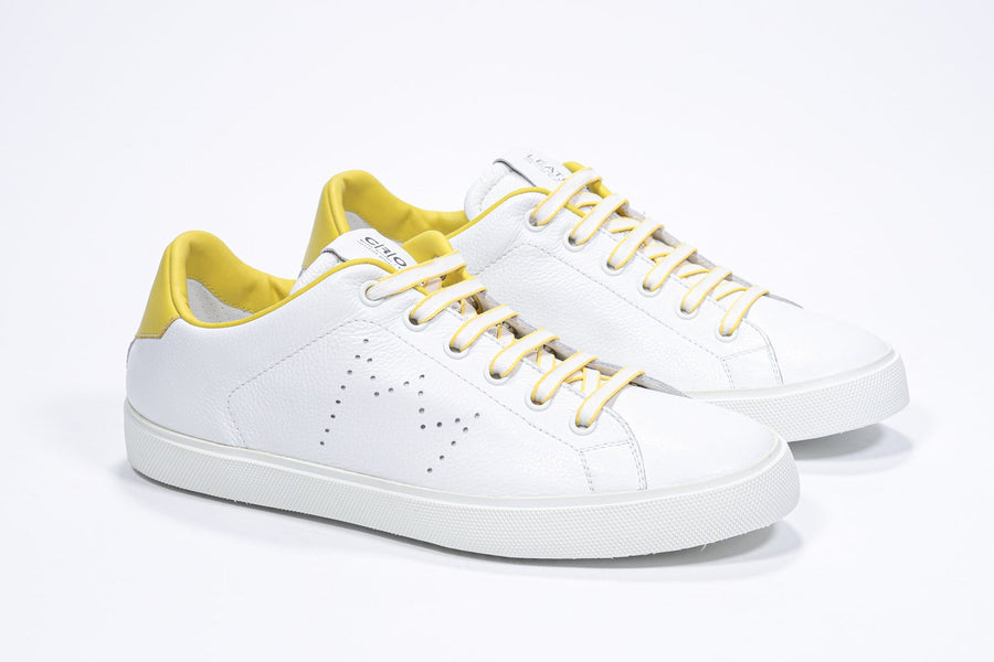 Three quarter front view of low top white sneaker with yellow detailing and perforated crown logo on upper. Full leather upper and white rubber sole.