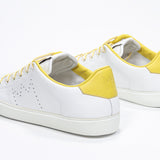 Three quarter back view of low top white sneaker with yellow detailing and perforated crown logo on upper. Full leather upper and white rubber sole.