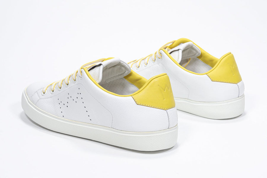 Three quarter back view of low top white sneaker with yellow detailing and perforated crown logo on upper. Full leather upper and white rubber sole.