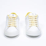 Front view of low top white sneaker with yellow detailing and perforated crown logo on upper. Full leather upper and white rubber sole.