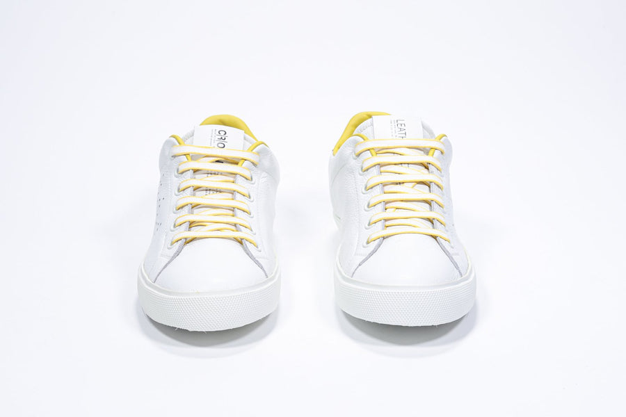 Front view of low top white sneaker with yellow detailing and perforated crown logo on upper. Full leather upper and white rubber sole.