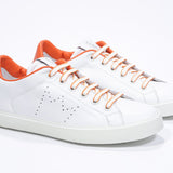 Three quarter front view of low top white sneaker with orange detailing and perforated crown logo on upper. Full leather upper and white rubber sole.