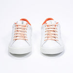 Front view of low top white sneaker with orange detailing and perforated crown logo on upper. Full leather upper and white rubber sole.