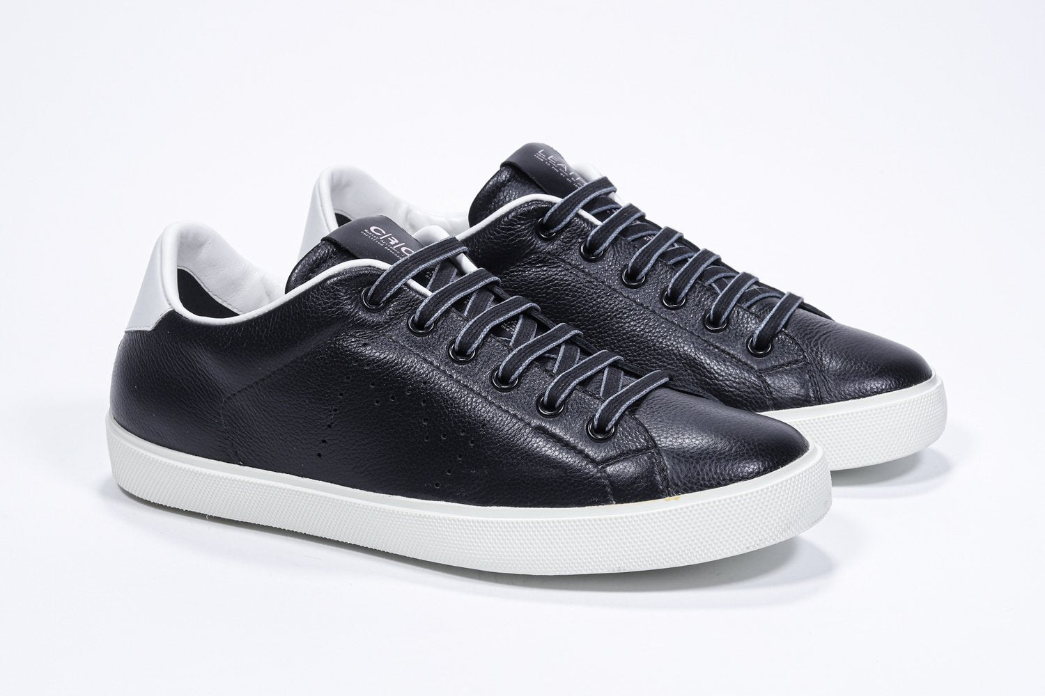 Three quarter front view of low top black sneaker with white detailing and perforated crown logo on upper. Full leather upper and white rubber sole.