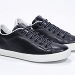 Three quarter front view of low top black sneaker with white detailing and perforated crown logo on upper. Full leather upper and white rubber sole.