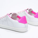 Three quarter back view of low top white sneaker with neon pink detailing and perforated crown logo on upper. Full leather upper and white rubber sole.