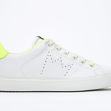 Side profile of low top white sneaker with neon yellow detailing and perforated crown logo on upper. Full leather upper and white rubber sole.