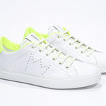 Three quarter front view of low top white sneaker with neon yellow detailing and perforated crown logo on upper. Full leather upper and white rubber sole.