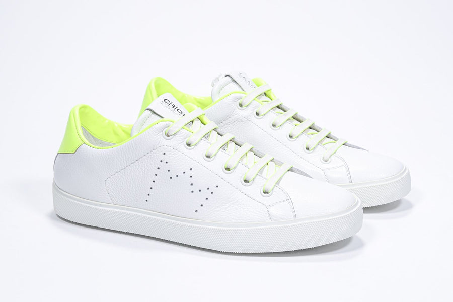 Three quarter front view of low top white sneaker with neon yellow detailing and perforated crown logo on upper. Full leather upper and white rubber sole.