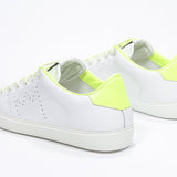 Three quarter back view of low top white sneaker with neon yellow detailing and perforated crown logo on upper. Full leather upper and white rubber sole.