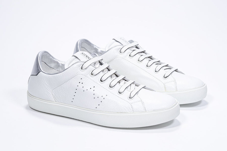 Three quarter front view of low top white sneaker with silver detailing and perforated crown logo on upper. Full leather upper and white rubber sole.