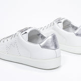 Three quarter back view of low top white sneaker with silver detailing and perforated crown logo on upper. Full leather upper and white rubber sole.