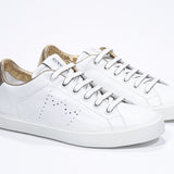 Three quarter front view of low top white sneaker with gold detailing and perforated crown logo on upper. Full leather upper and white rubber sole.