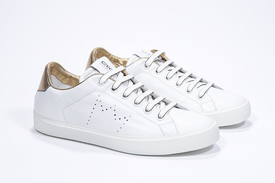 Three quarter front view of low top white sneaker with gold detailing and perforated crown logo on upper. Full leather upper and white rubber sole.