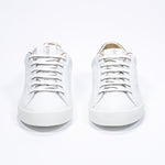 Front view of low top white sneaker with gold detailing and perforated crown logo on upper. Full leather upper and white rubber sole.