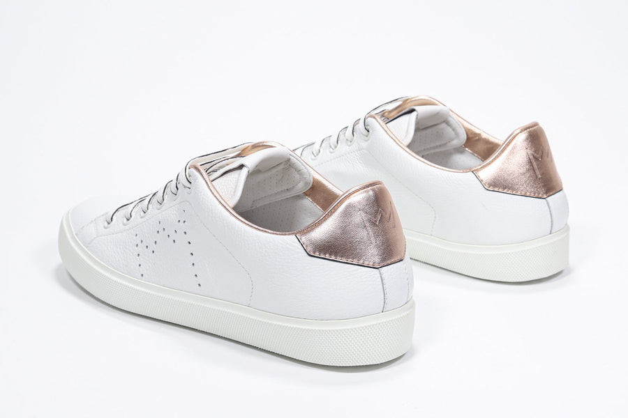 Three quarter back view of low top white sneaker with rose gold metallic detailing and perforated crown logo on upper. Full leather upper and white rubber sole.