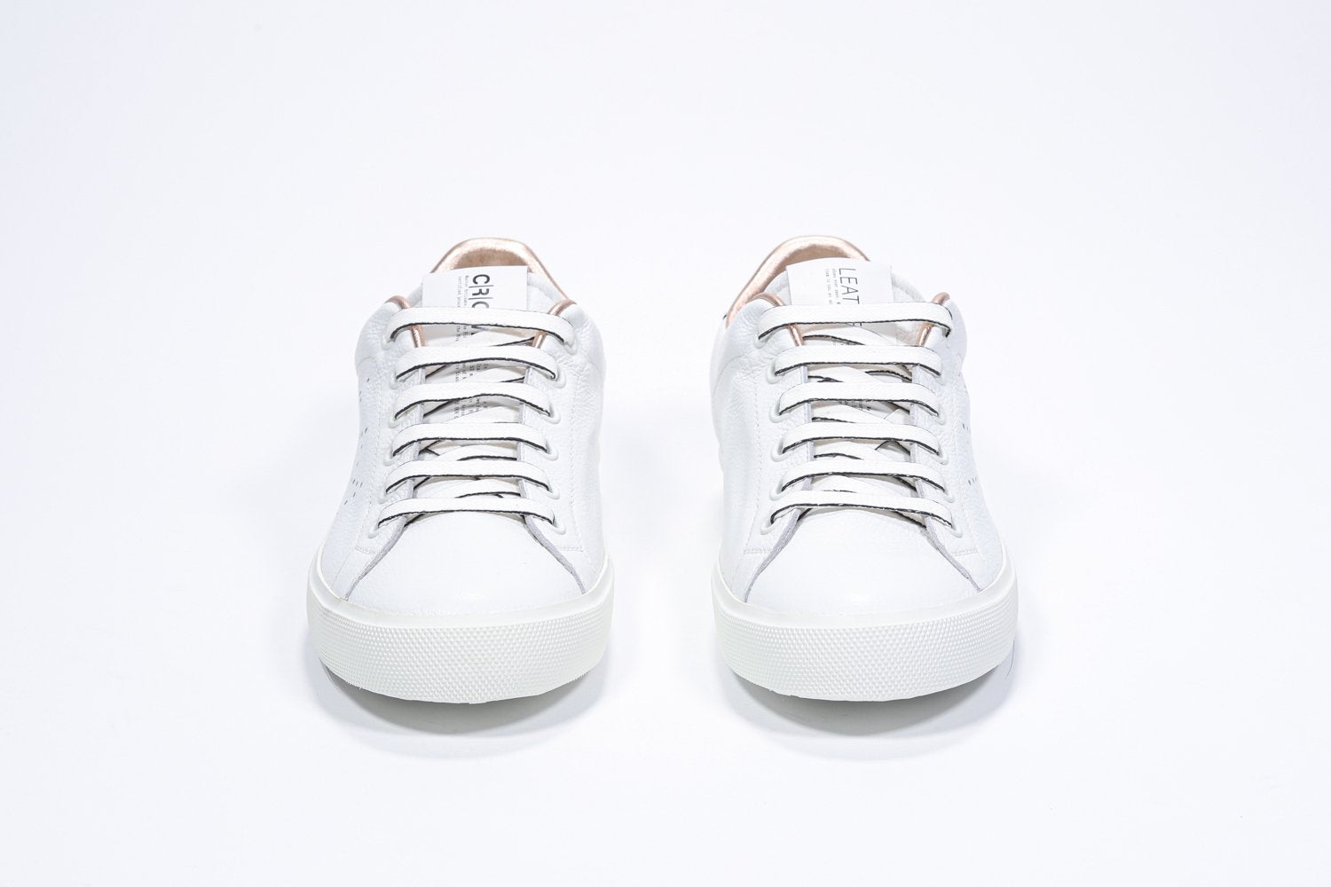 Vue de face de la chaussure blanche sneaker avec des détails métalliques or rose et le logo perforé de la couronne sur la tige. Tige en cuir et semelle en caoutchouc blanc.