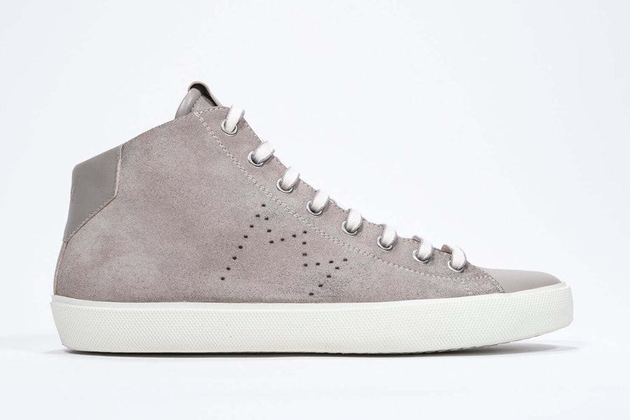 Side profile of mid top beige sneaker with full suede upper with perforated crown logo, internal zip and white sole.