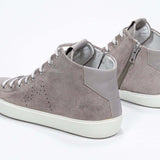 Three quarter back view of mid top beige sneaker with full suede upper with perforated crown logo, internal zip and white sole.