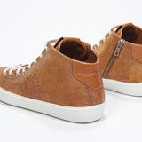 Three quarter back view of mid top rust sneaker with full suede upper with perforated crown logo, internal zip and white sole.