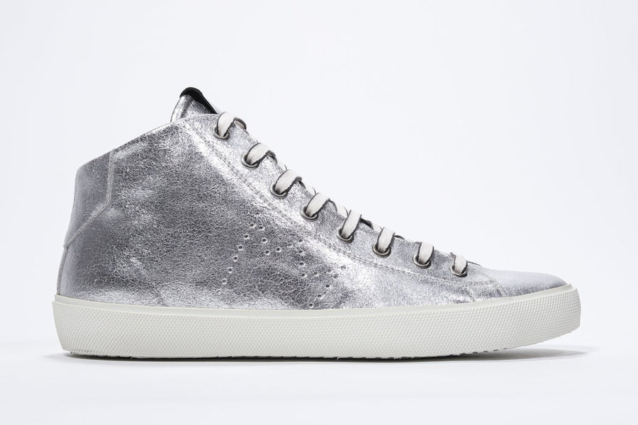 Side profile of mid top silver sneaker with full leather upper with perforated crown logo, internal zip and white sole.