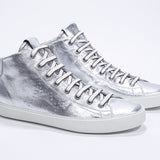 Three quarter front view of mid top silver sneaker with full leather upper with perforated crown logo, internal zip and white sole.