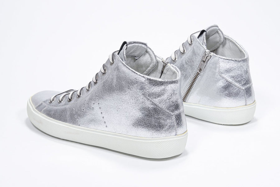 Three quarter back view of mid top silver sneaker with full leather upper with perforated crown logo, internal zip and white sole.