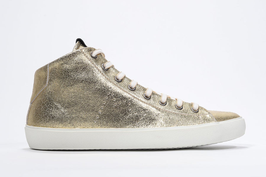 Side profile of mid top gold sneaker with full leather upper with perforated crown logo, internal zip and white sole.