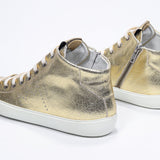 Three quarter back view of mid top gold sneaker with full leather upper with perforated crown logo, internal zip and white sole.