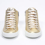 Front view of mid top gold sneaker with full leather upper with perforated crown logo, internal zip and white sole.