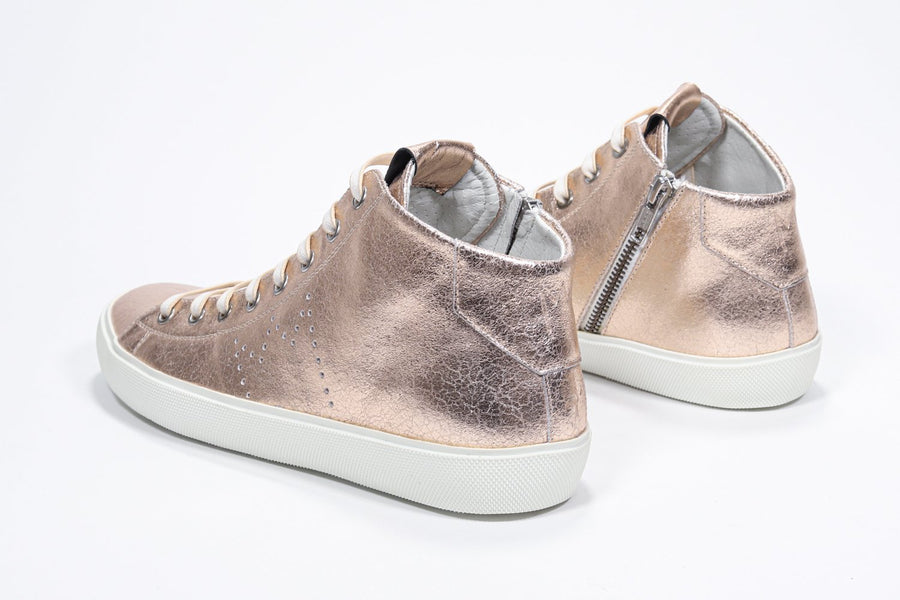 Three quarter back view of mid top rose-gold sneaker with full leather upper with perforated crown logo, internal zip and white sole.