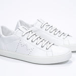 Three quarter front view of low top white sneaker with perforated crown logo on upper. Full leather upper and white rubber sole.