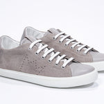 Three quarter front view of low top beige sneaker with perforated crown logo on upper. Full suede upper and white rubber sole.