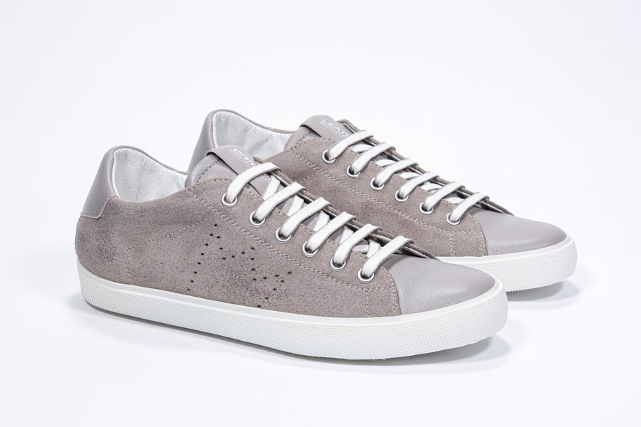Three quarter front view of low top beige sneaker with perforated crown logo on upper. Full suede upper and white rubber sole.