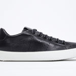 Side profile of low top black sneaker with perforated crown logo on upper. Full leather upper and white rubber sole.