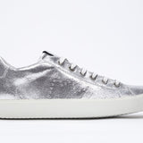 Side profile of low top silver sneaker with perforated crown logo on upper. Full metallic leather upper and white rubber sole.