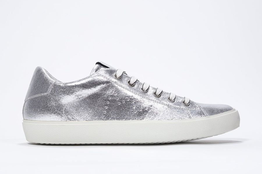 Side profile of low top silver sneaker with perforated crown logo on upper. Full metallic leather upper and white rubber sole.